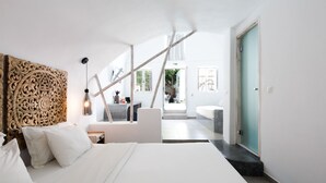 Une chambre d’hôtel moderne avec un grand lit, une tête de lit en bois, un bureau et une vue sur la salle de bain et l’espace extérieur.