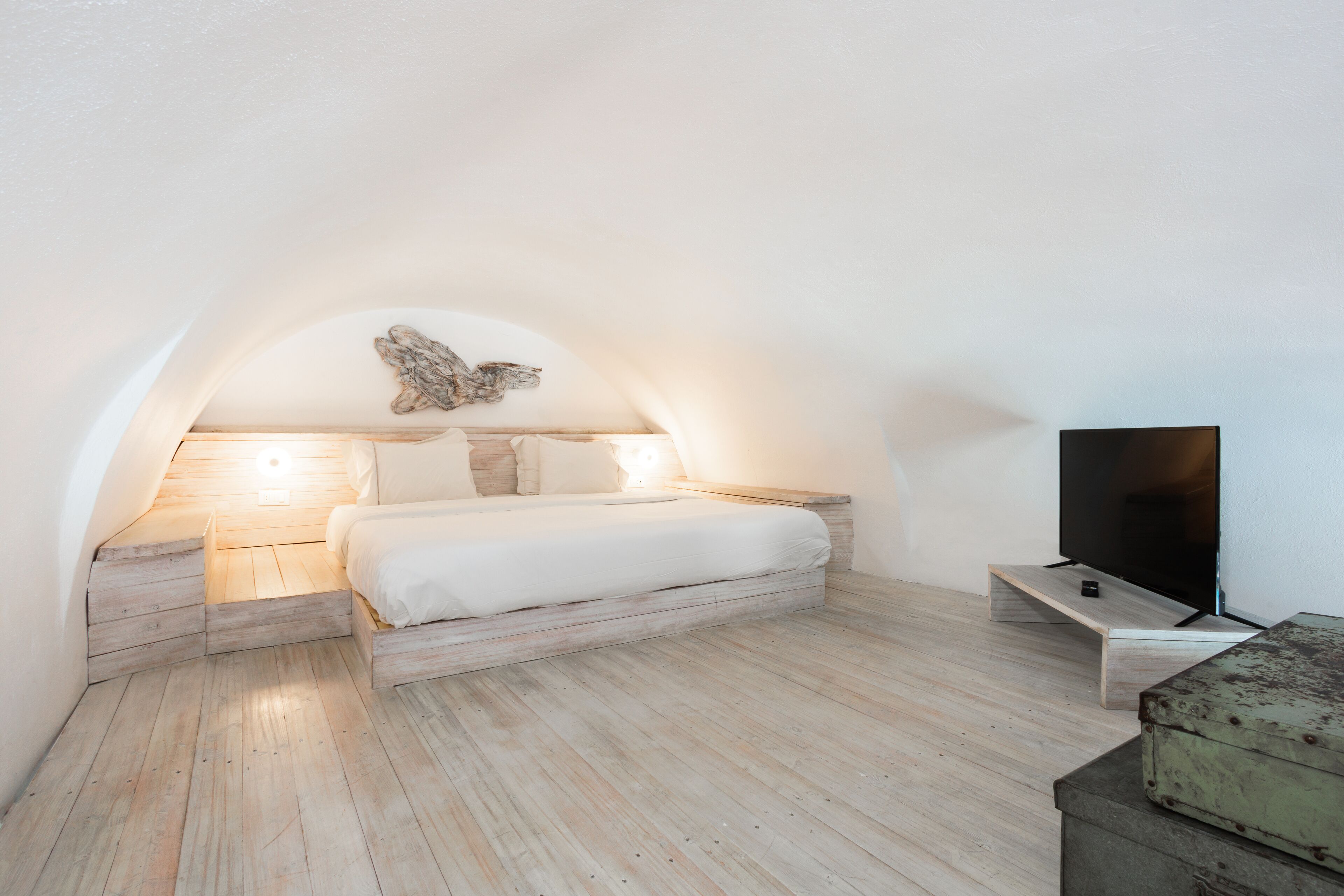 A bedroom with a wooden floor, a bed with white bedding, a wall-mounted TV, and a decorative butterfly on the wall.