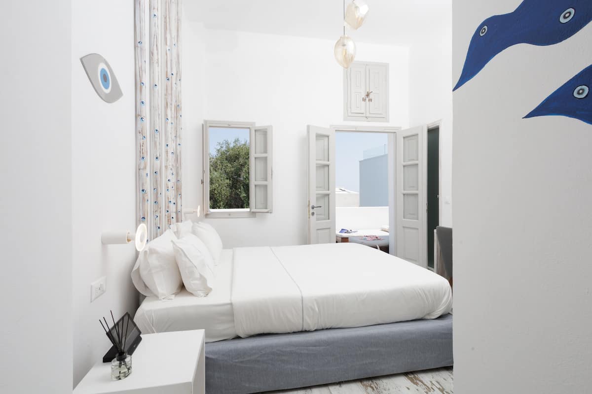 A bedroom with a bed, bedside table, and a window with a view of greenery.