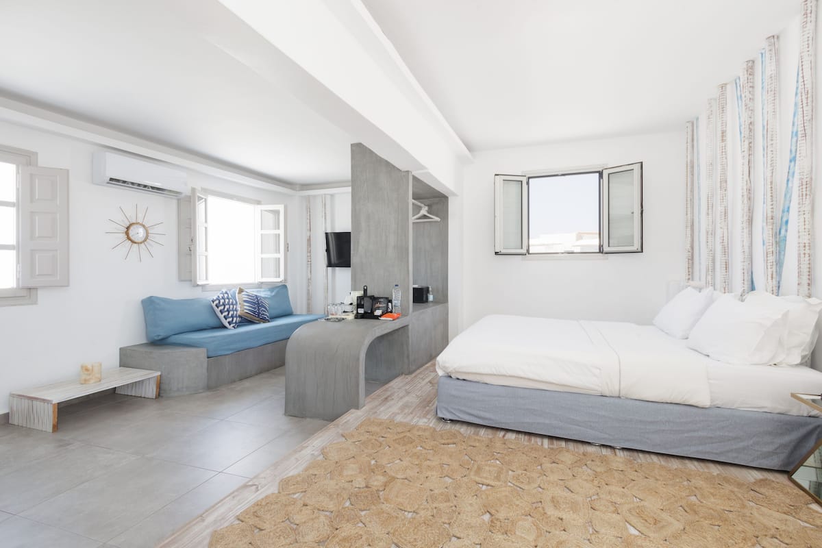 A modern bedroom with a bed, a seating area with a sofa and a coffee table, a television, and a large window with curtains.