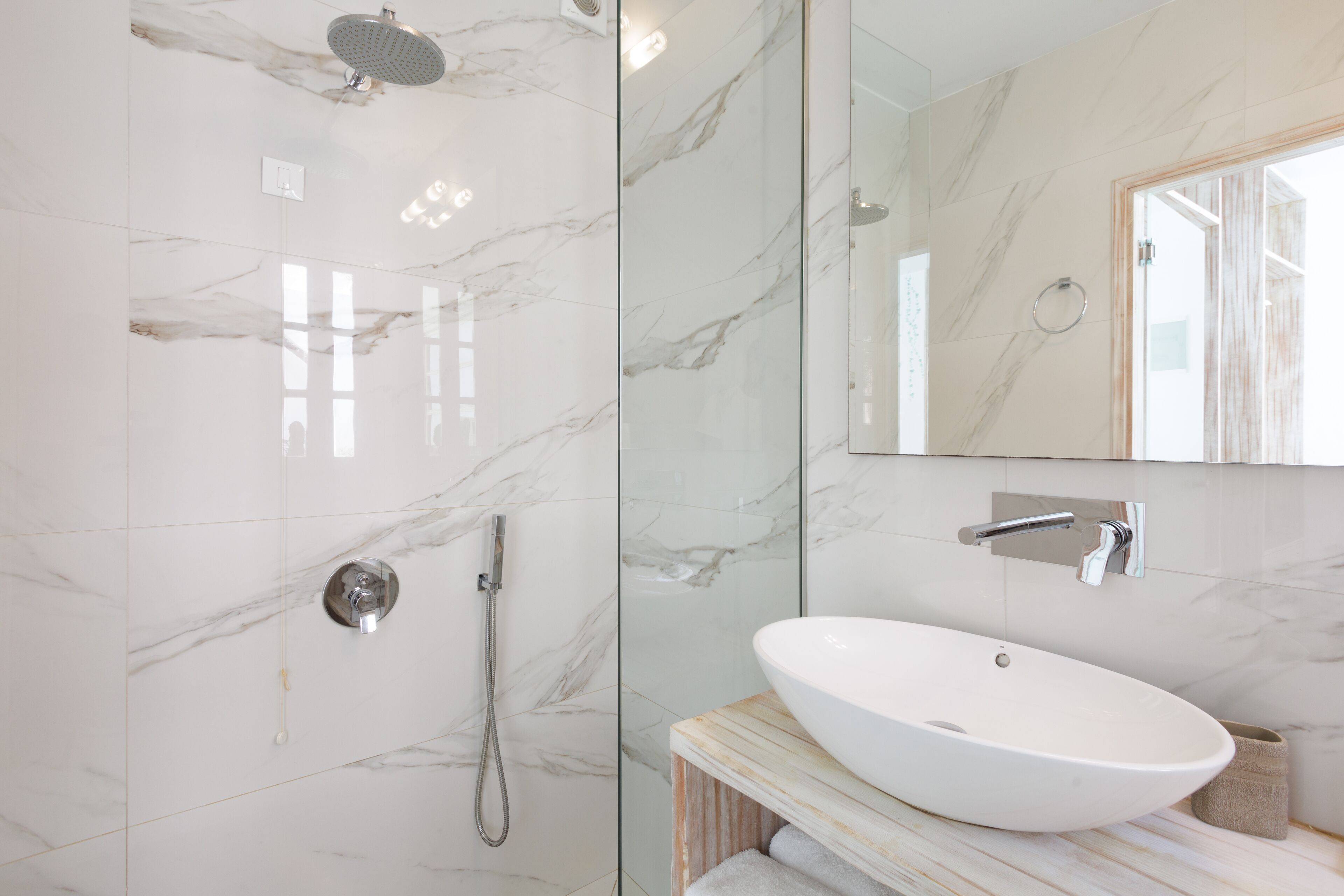 A modern bathroom with a glass-enclosed shower, a white sink, and a large mirror.