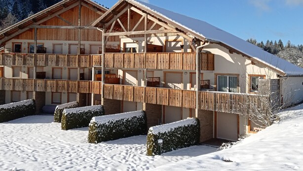 Eine Chalet mit mehreren Balkonen, Holzfassade und verschneiter Umgebung.
