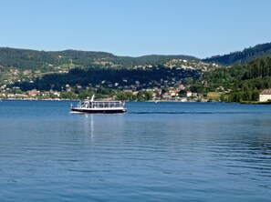 A boat on a calm lake with a town and hills in the background. - Les Agapanthes *** Lakeside Apartment (Gérardmer)