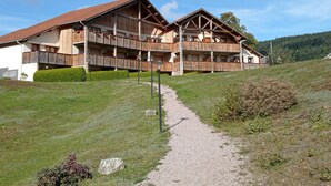Ein mehrgeschossiges Holzgebäude mit Balkonen, einem Kiesweg, der zum Eingang führt, und einer hügeligen Landschaft im Hintergrund.