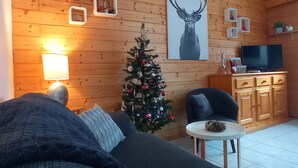 Ein gemütliches Wohnzimmer mit Holzwand, Weihnachtsbaum, Sofa, Fernseher und Schrank.