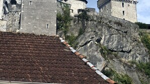 Un château historique en pierre, doté de nombreuses tours et d’une tourelle, situé sur une colline rocheuse et coiffé d’un toit en tuiles.