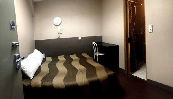 Une chambre d’hôtel avec un lit, un bureau, une chaise, un téléphone et une porte.