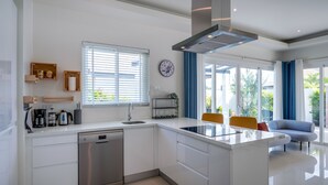 Una cocina moderna equipada con lavavajillas, cafetera y hervidor. Cuenta con una zona de comedor con mesa y sillas.