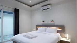 Una habitación de hotel moderna con una cama grande, una mesita de noche con lámpara, un aire acondicionado y vistas al exterior.