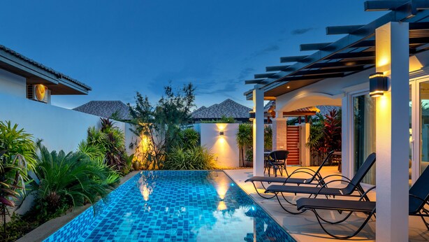Una piscina con sillones de descanso y una pérgola, rodeada de plantas tropicales.