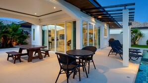 Un patio exterior con mesa y sillas para comer, una piscina y una zona de estar cubierta.