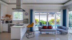 Cocina moderna con isla central, taburetes de bar y zona de comedor con sofá gris y cojines rojos.