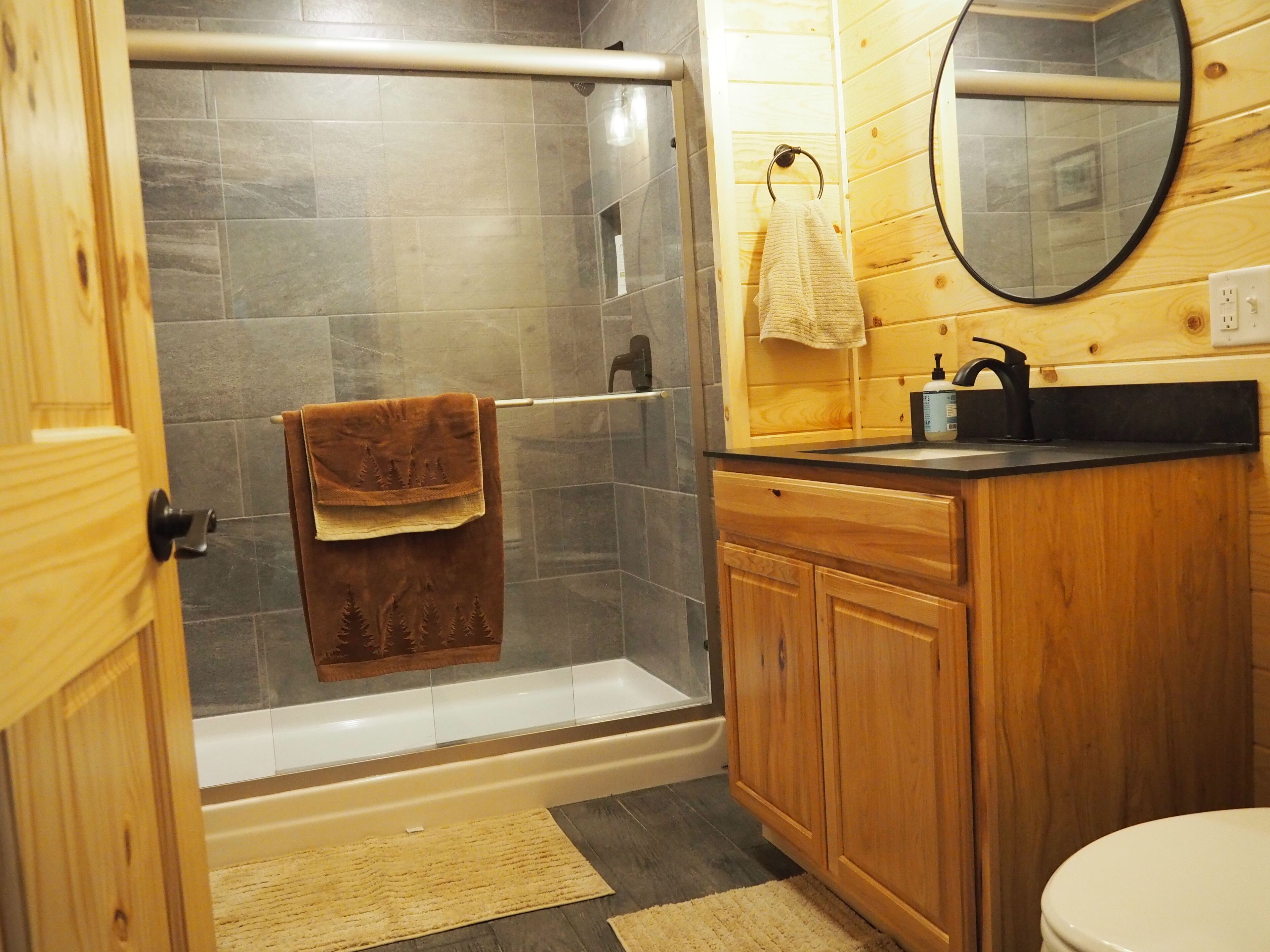 A bathroom with a shower, toilet, and wooden cabinets.