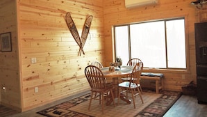 A wooden cabin interior with a dining table, chairs, a window, and a fireplace. - Enjoy privacy in this newly built cabin with spectacular view of North Star Lake (Marcell)