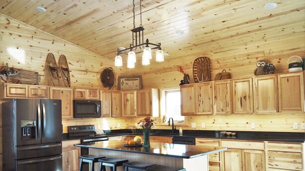 A spacious kitchen with wooden cabinets, a stainless steel refrigerator, a microwave, and a large island with bar stools. - Enjoy privacy in this newly built cabin with spectacular view of North Star Lake (Marcell)