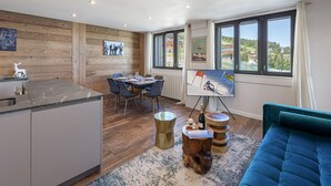 A modern kitchen with a dining area, wooden walls, and large windows with a view of the Alps.