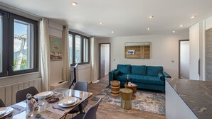 A modern living room with a teal sofa, a dining area with a glass table, and a view of mountains through large windows.