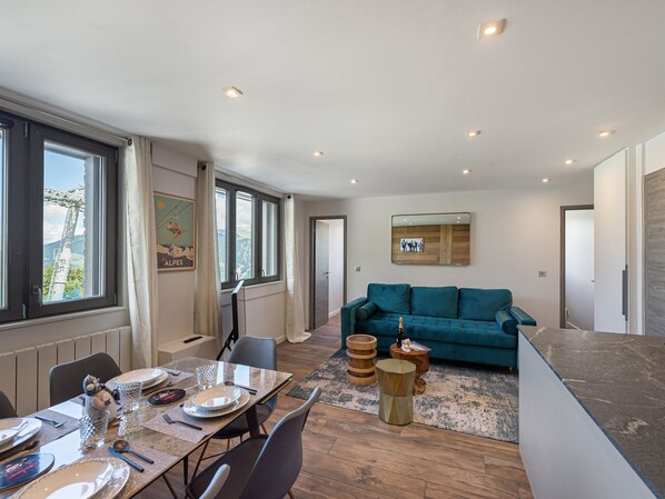 Una sala de estar moderna con un sofá color turquesa, un comedor con mesa de vidrio y vistas a montañas a través de amplios ventanales.