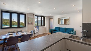 A modern kitchen with a large island, a dining area with a table and chairs, and a teal sofa.