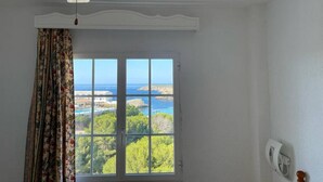 Habitación con un ventanal que ofrece vistas a un paisaje costero, un ventilador de techo y una puerta con pomo blanco.