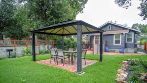 A covered patio with a table and chairs, surrounded by a well-maintained lawn and a stone border.