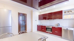 A modern kitchen with stainless steel appliances, red cabinetry, and a dining area with a white table and metal chairs. - MinskLux Apartments 2 bedrooms - 100 sqm (Minsk)