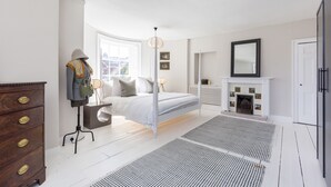 Ein Schlafzimmer mit Bett, Schminktisch, Spiegel, Kamin und Stehlampe.