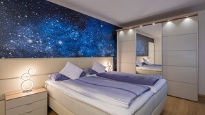 Une chambre à coucher avec une fresque représentant un ciel étoilé au plafond, un lit avec une literie blanche et bleue, une table de chevet avec un miroir et un plancher en bois.