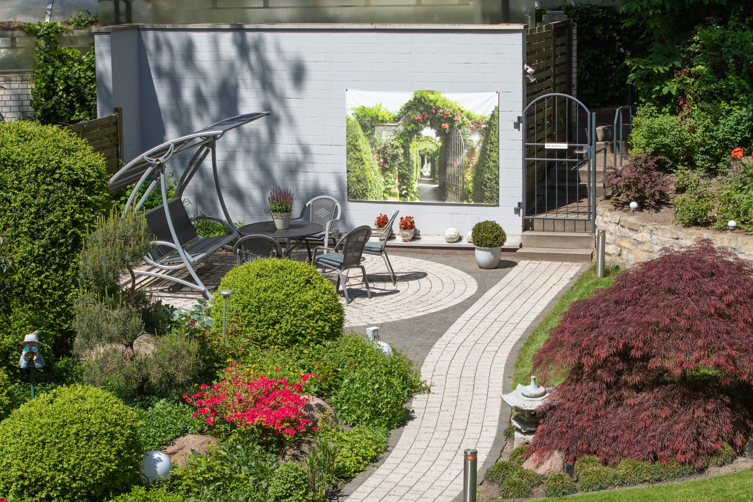 Une terrasse de jardin avec un mur blanc, une fresque murale et un chemin.