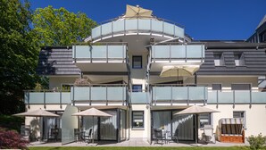 Un immeuble moderne à plusieurs étages, doté de balcons, d’un espace extérieur aménagé pour s’asseoir et d’une terrasse couverte.