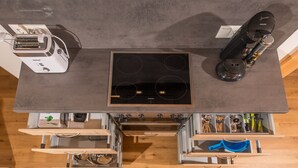 A modern kitchen with a built-in stove, a coffee maker, and various utensils in drawers. - Ferienwohnung (Lenggries)