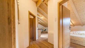 A narrow hallway with wooden flooring and a sloped ceiling. A door leads to a room with a bed and a desk. - Ferienwohnung (Lenggries)