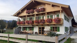 A traditional chalet with multiple balconies adorned with flower boxes, a stone facade, and a wooden deck in front. - Ferienwohnung (Lenggries)