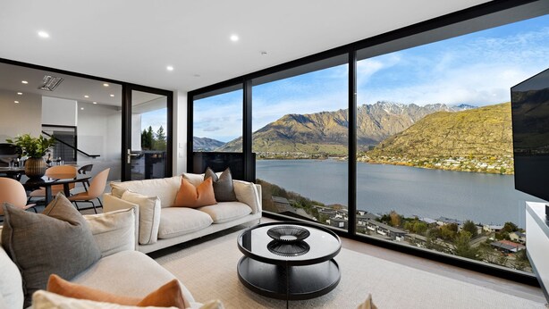 A modern living room with a large window overlooking a lake and mountains.