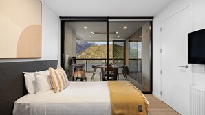 A bedroom with a bed, a TV, a balcony with a table and chairs, and a mountain view.