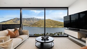 A modern living room with a large window offering a scenic mountain view, a flat-screen TV, and a minimalist coffee table.