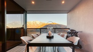 Espaço de refeições com mesa, cadeiras, churrasqueira e vista para montanhas.