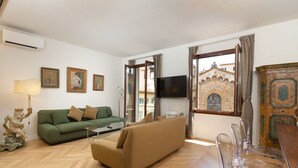 A living room with a green sofa, a tan sofa, a TV, and a dining area with clear chairs.