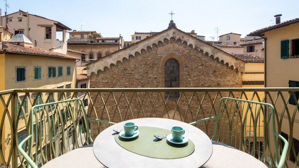 A balcony with a table and chairs, overlooking a historic building with a cross on top.