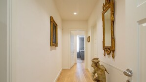 A hallway with a wooden floor, a statue, and two large mirrors on the walls.