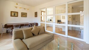 A modern living room with a sofa, clear chairs, a piano, and a glass table.