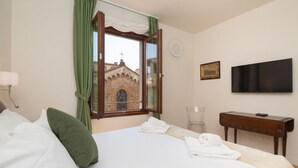 A hotel room with a bed, a TV, a desk, and a window with curtains.