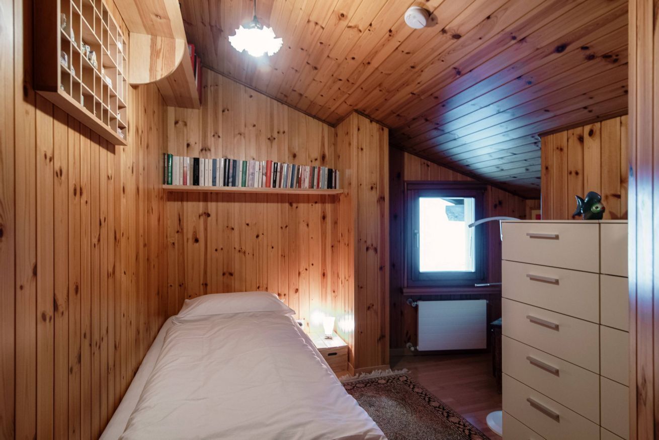 A wooden-paneled room with a bed, a dresser, a shelf with books, and a window.
