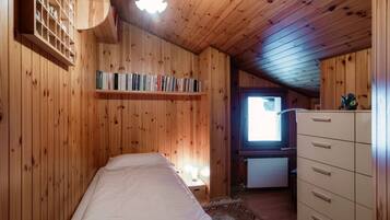 A wooden-paneled room with a bed, a dresser, a shelf with books, and a window.