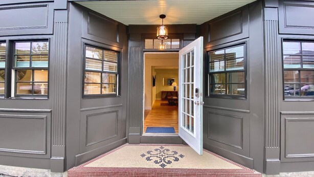 A house entrance with a dark gray exterior, a white door, and a small porch area with a patterned doormat. - Recently Renovated 2 Bed 1 Bath (Dog Friendly) Apartment in the Broadway Neighborhood (Newport)