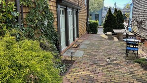 A narrow brick pathway leading to a wooden house with a green door, surrounded by greenery and a small table with chairs. - Recently Renovated 2 Bed 1 Bath (Dog Friendly) Apartment in the Broadway Neighborhood (Newport)