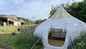 A white tent with a conical roof, set up in a grassy area with a wooden bench and a barbecue grill nearby. - Star Gazing Bell Tent Farm Stay (Loughborough)