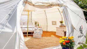 A tent with a bed, dresser, and a basket with flowers. - Star Gazing Bell Tent Farm Stay (Loughborough)