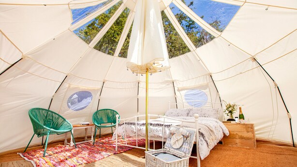 A spacious tent with a bed, two chairs, a small table, and a basket. - Star Gazing Bell Tent Farm Stay (Loughborough)