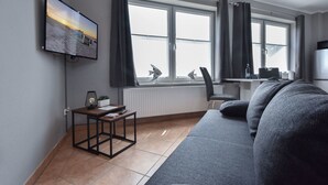 A modern living room with a large window, a flat-screen TV, a sofa, a small table, and a radiator.